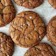 Several large, brown, crackly cookies arranged on a marble surface. The cookies have a glossy appearance with a few white specks on top.