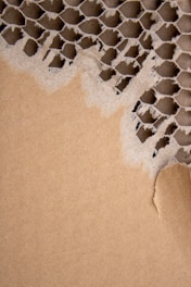 A piece of corrugated cardboard with layers exposed, displaying its distinctive honeycomb pattern. The section on the right is torn, revealing the structured texture beneath the outer layer.