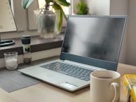 A modern workspace with a lit soy candle beside a laptop and a cup of tea.