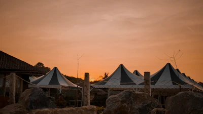 A peaceful sunset over a rural festival with tents and string lights glowing warmly.