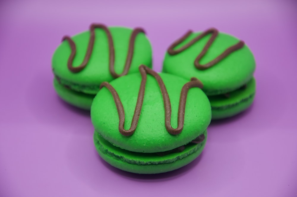 three green macaroons with chocolate icing on a purple surface