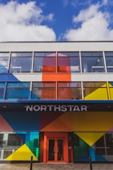 A modern building facade featuring bold geometric patterns in bright colors such as blue, red, yellow, and orange. Large windows dominate the upper floors, and the entrance is marked by the word 'NORTHSTAR' above a red door.