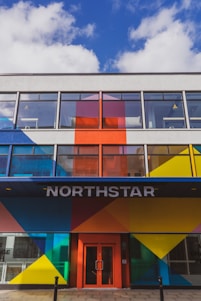 A modern building facade featuring bold geometric patterns in bright colors such as blue, red, yellow, and orange. Large windows dominate the upper floors, and the entrance is marked by the word 'NORTHSTAR' above a red door.
