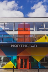 A modern building facade featuring bold geometric patterns in bright colors such as blue, red, yellow, and orange. Large windows dominate the upper floors, and the entrance is marked by the word 'NORTHSTAR' above a red door.