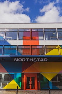 A modern building facade featuring bold geometric patterns in bright colors such as blue, red, yellow, and orange. Large windows dominate the upper floors, and the entrance is marked by the word 'NORTHSTAR' above a red door.