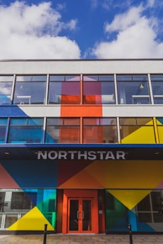A modern building facade featuring bold geometric patterns in bright colors such as blue, red, yellow, and orange. Large windows dominate the upper floors, and the entrance is marked by the word 'NORTHSTAR' above a red door.
