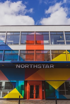 A modern building facade featuring bold geometric patterns in bright colors such as blue, red, yellow, and orange. Large windows dominate the upper floors, and the entrance is marked by the word 'NORTHSTAR' above a red door.