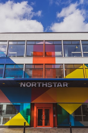 A modern building facade featuring bold geometric patterns in bright colors such as blue, red, yellow, and orange. Large windows dominate the upper floors, and the entrance is marked by the word 'NORTHSTAR' above a red door.