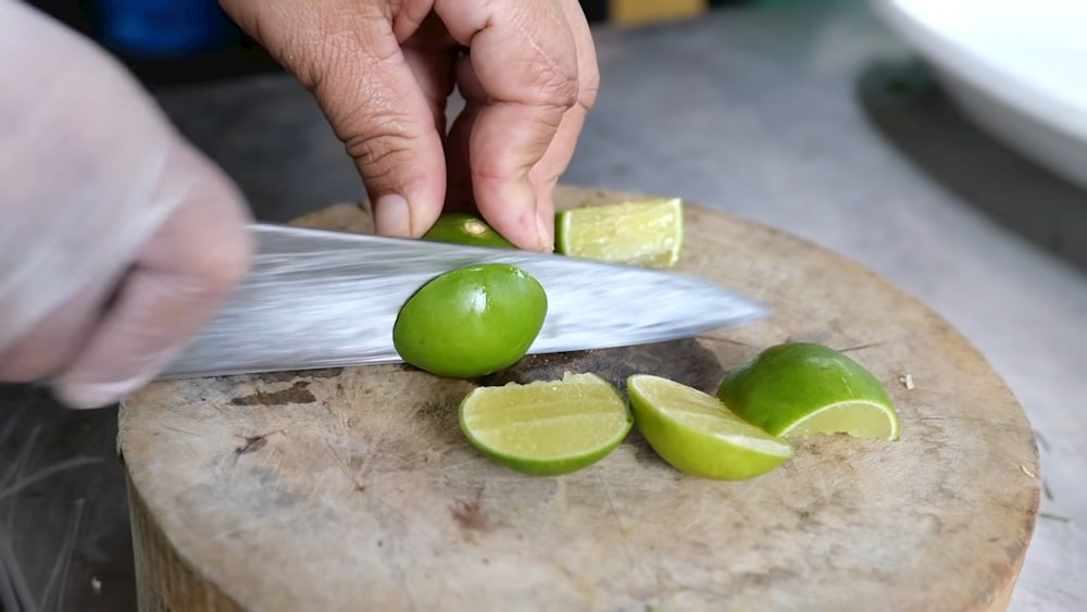 a person cutting limes with a knife on a cutting board