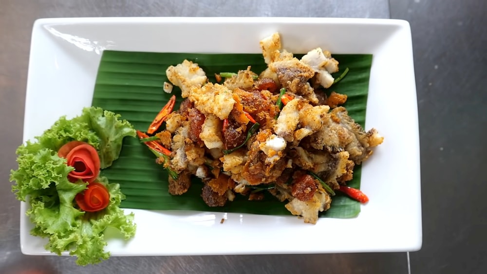 a white plate topped with fried food next to a green leaf