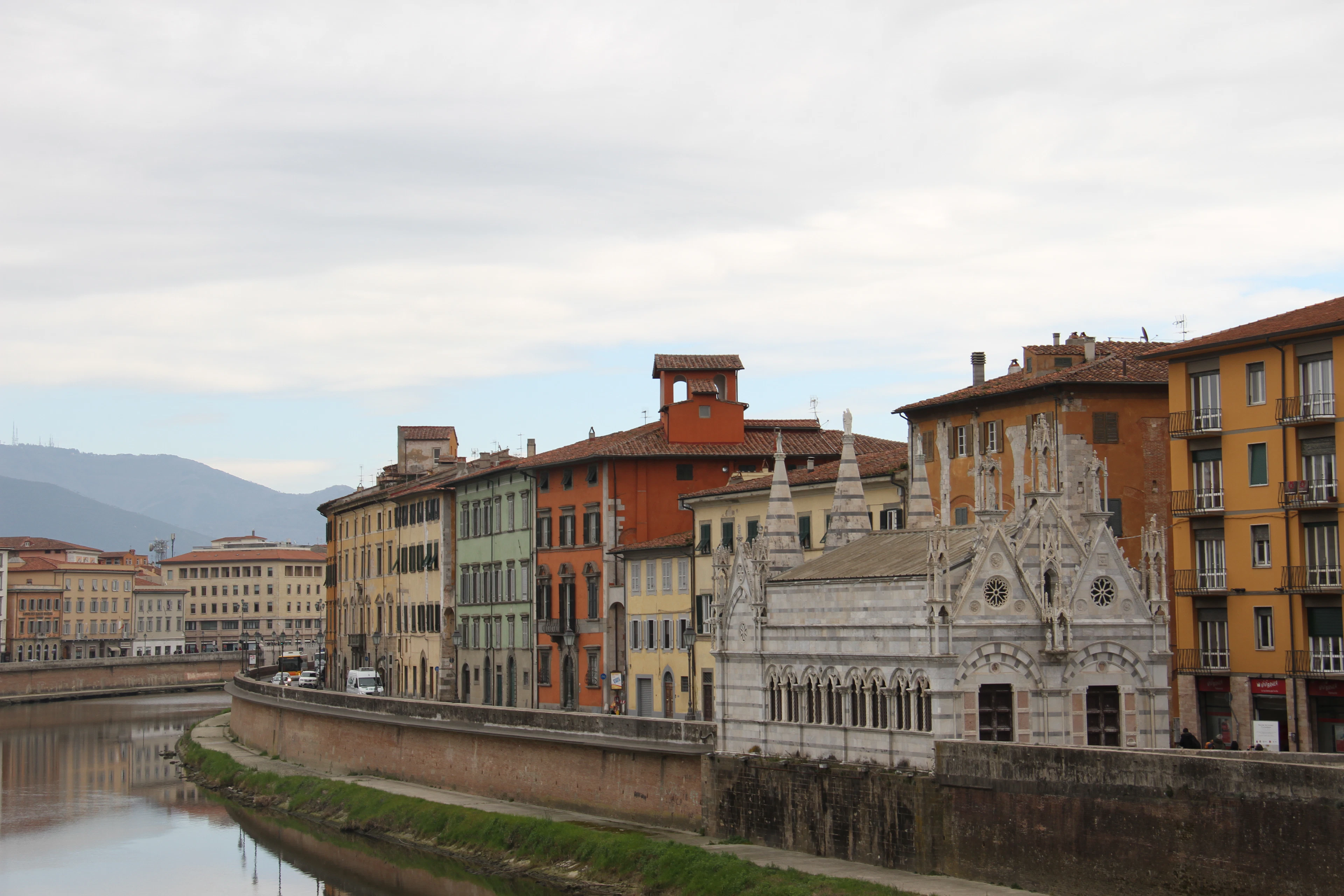 The Gothic Santa Maria della Spina church on the Arno riverbank in Pisa, flanked by colorful buildings.