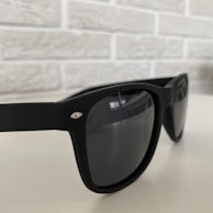 Black sunglasses with a glossy finish resting on a smooth white marble surface.