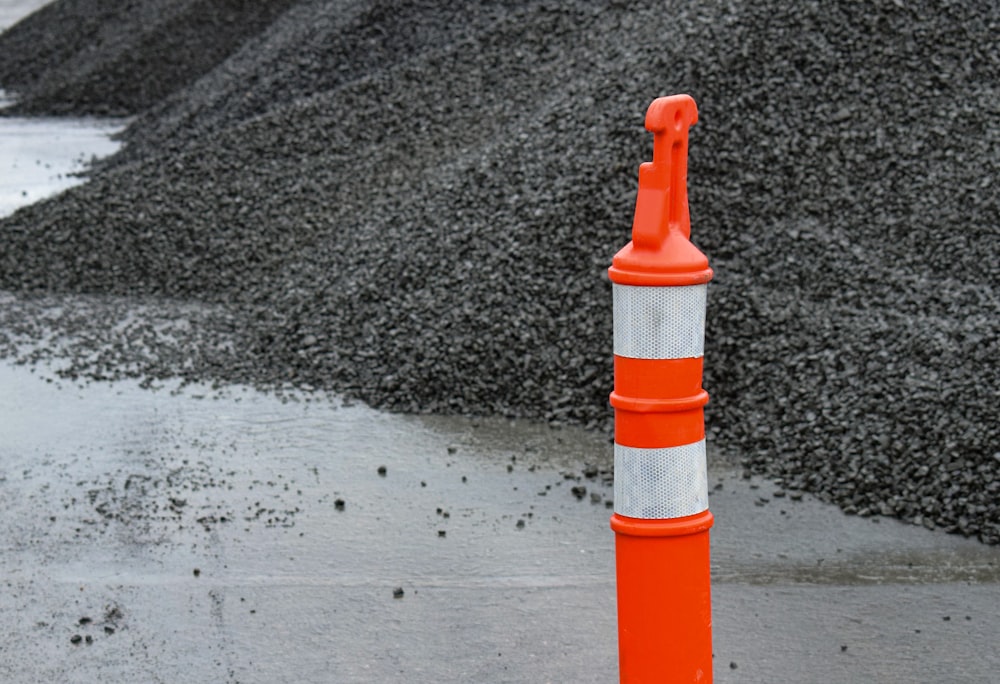 an orange and white traffic cone next to a pile of gravel