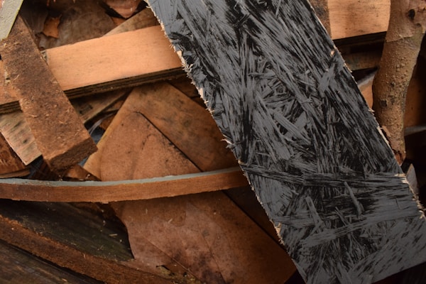A collection of wooden planks and plywood pieces, arranged in a haphazard manner. The textures of the wood vary, with one prominently featuring dark, intricate patterns typical of oriented strand board. The colors range from light brown to dark brown, with some areas appearing worn and rough.