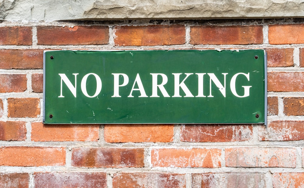 a green sign that says no parking on a brick wall