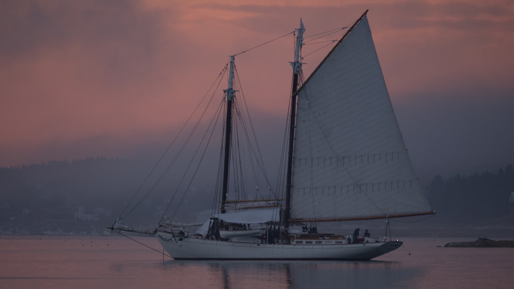 a sailboat in the water with a pink sky in the background