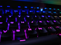 Close-up of a hacker-style keyboard with violet backlighting on a black desk.