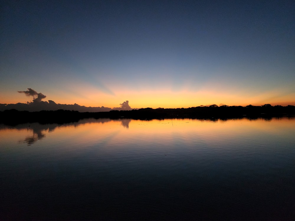 the sun is setting over a calm lake