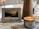 A decorative plaque with a motivational Christian message is propped up next to a lit nutmeg-scented candle on a patterned tablecloth. The plaque features a photograph of a serene landscape with mountains and trees during sunset. The overall setting is cozy and calm.