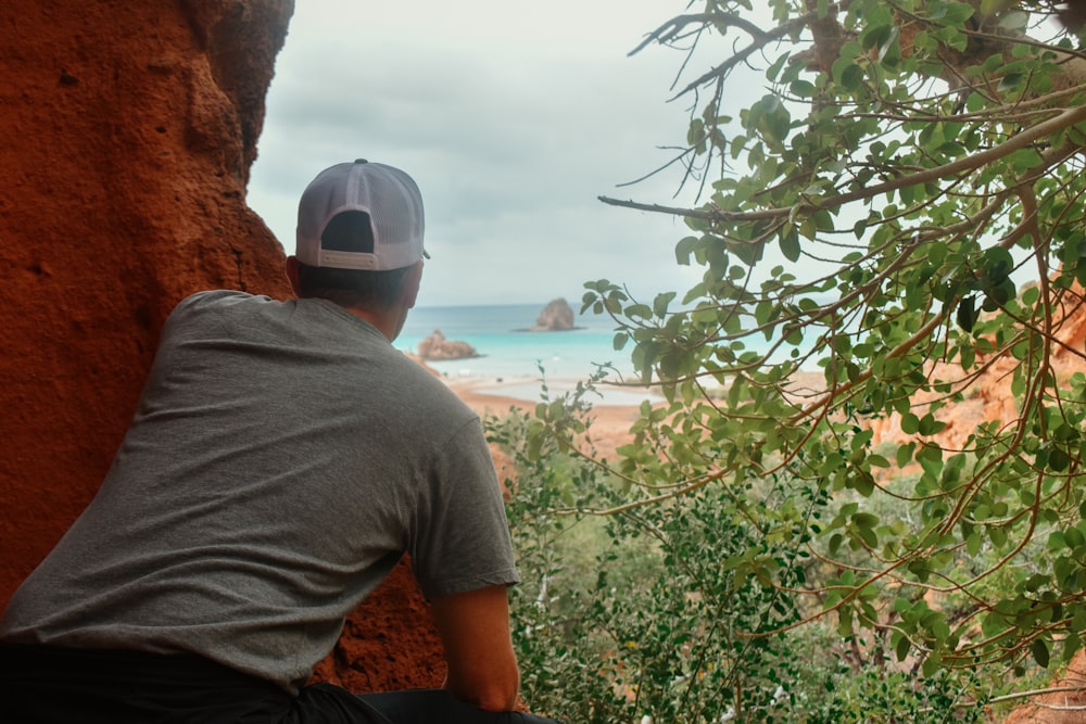 um homem sentado em cima de uma rocha ao lado do oceano