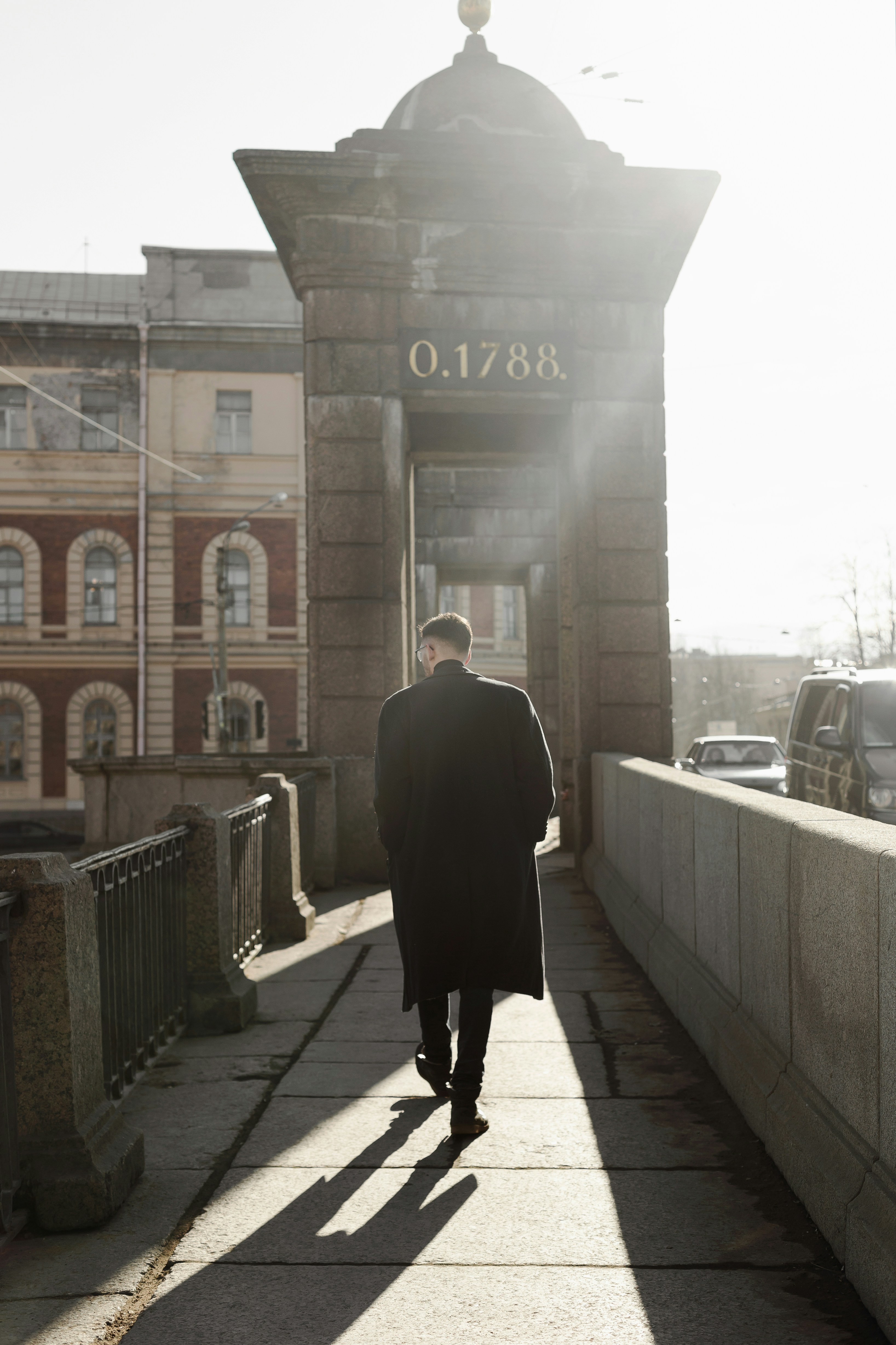 a man in a long coat walking across a bridge