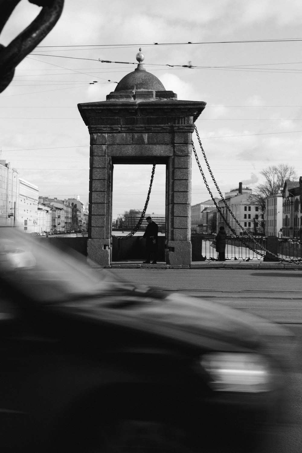 a black and white photo of a car passing by a bridge