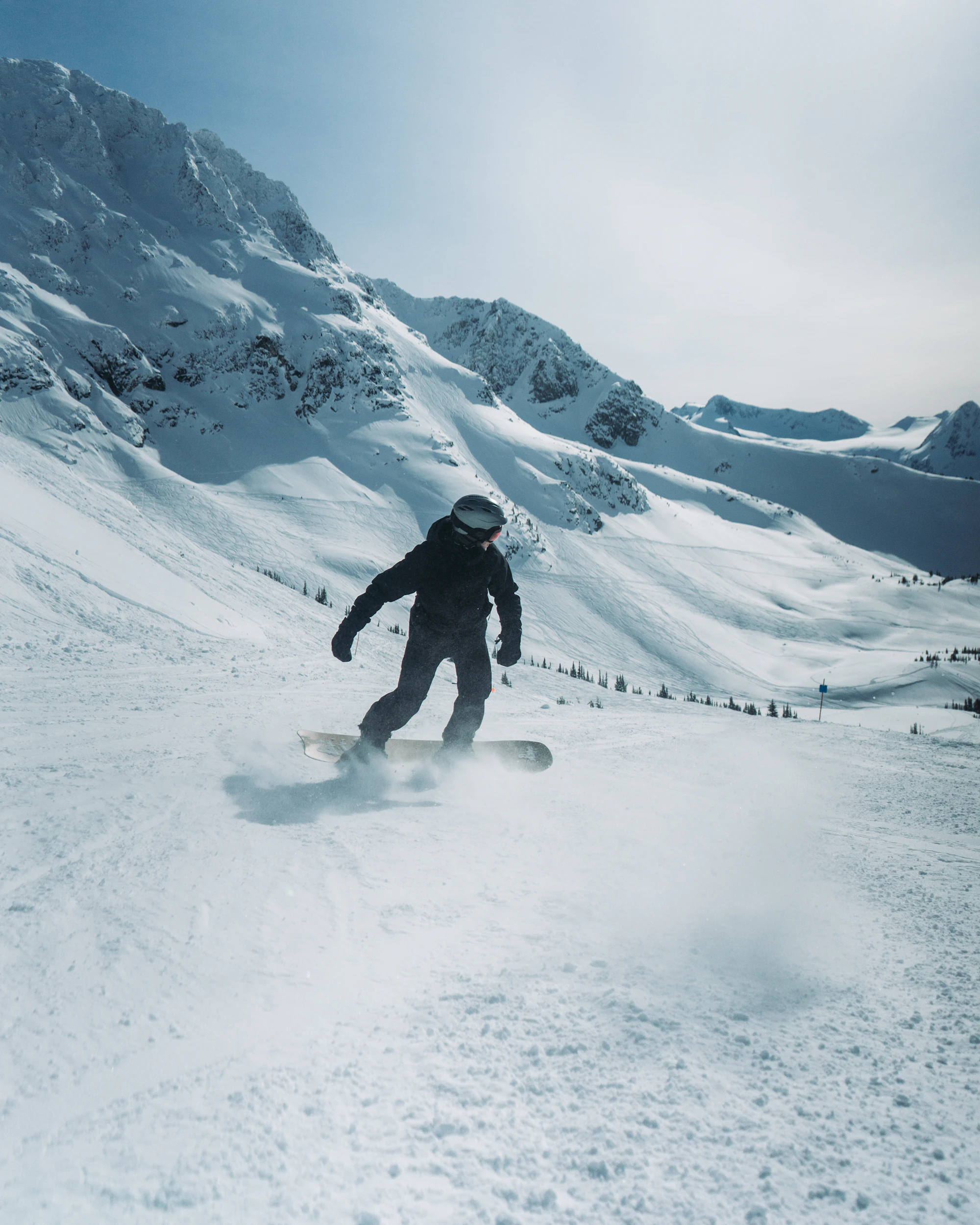 Snowboarder in black outerwear carving down a bright alpine slope