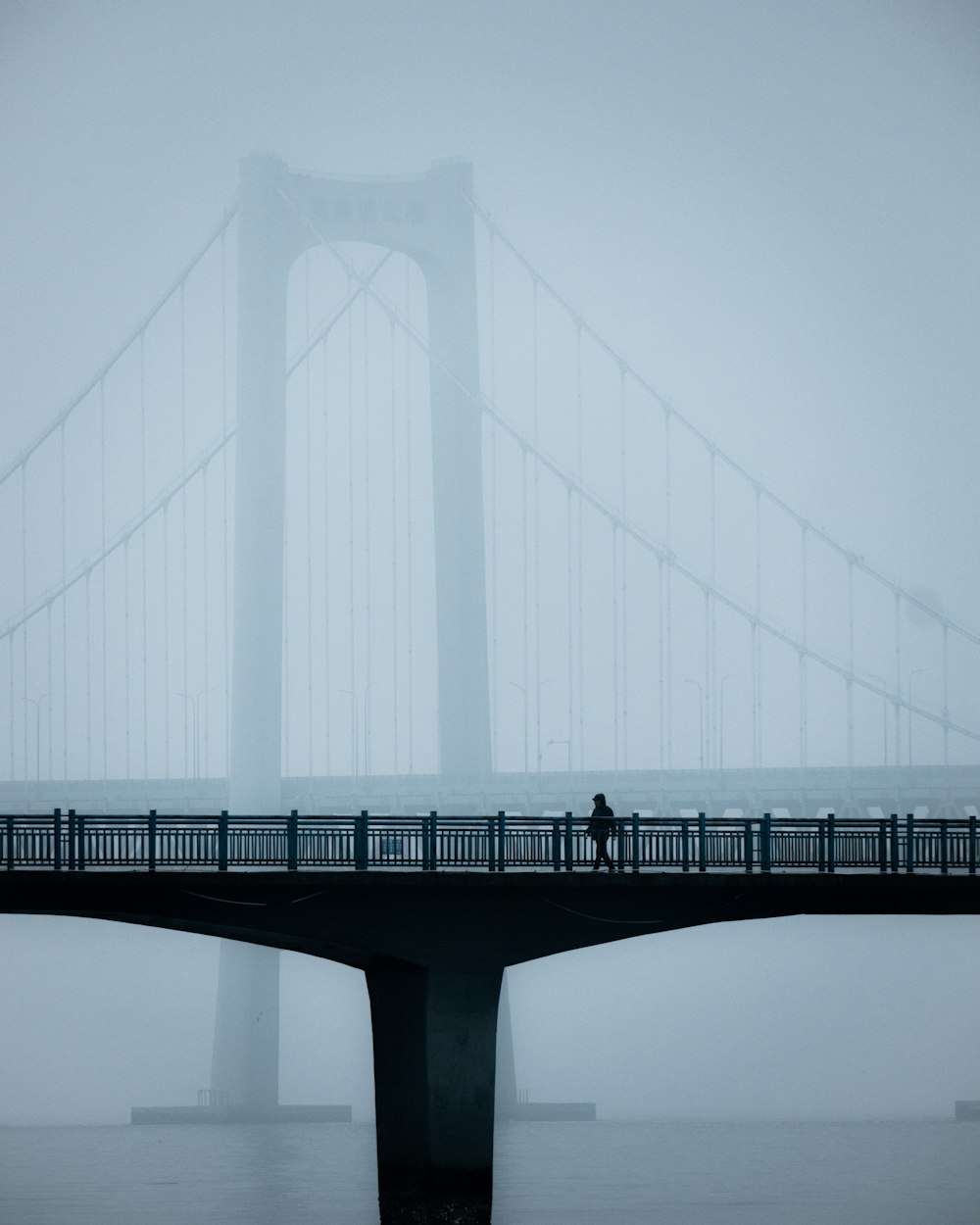 a person walking across a bridge on a foggy day