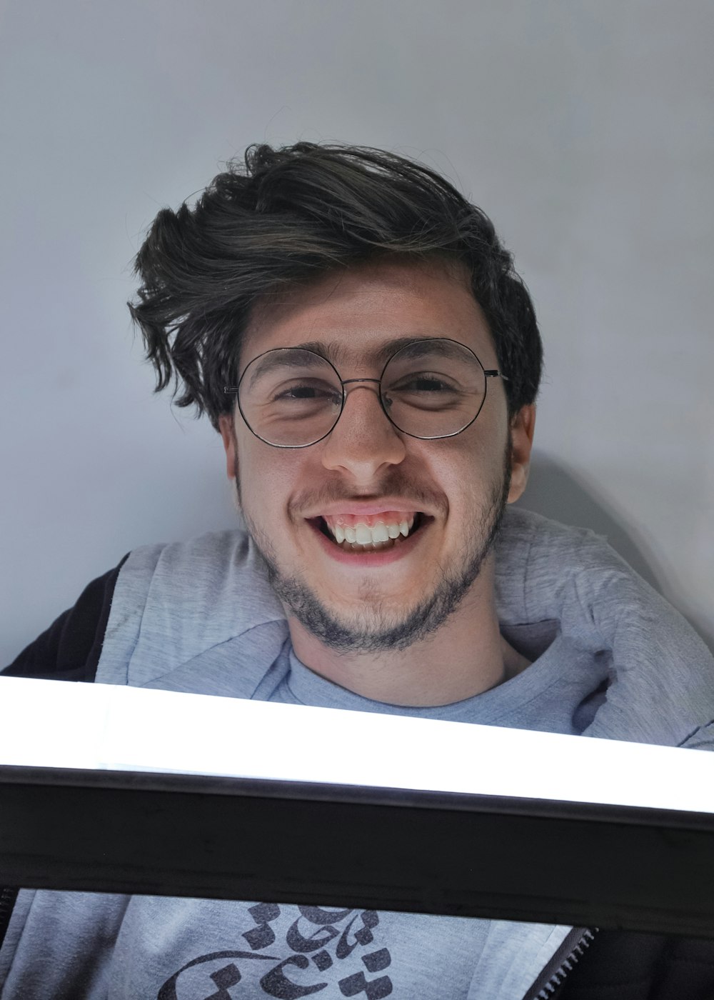 Un homme avec des lunettes et une chemise grise souriant