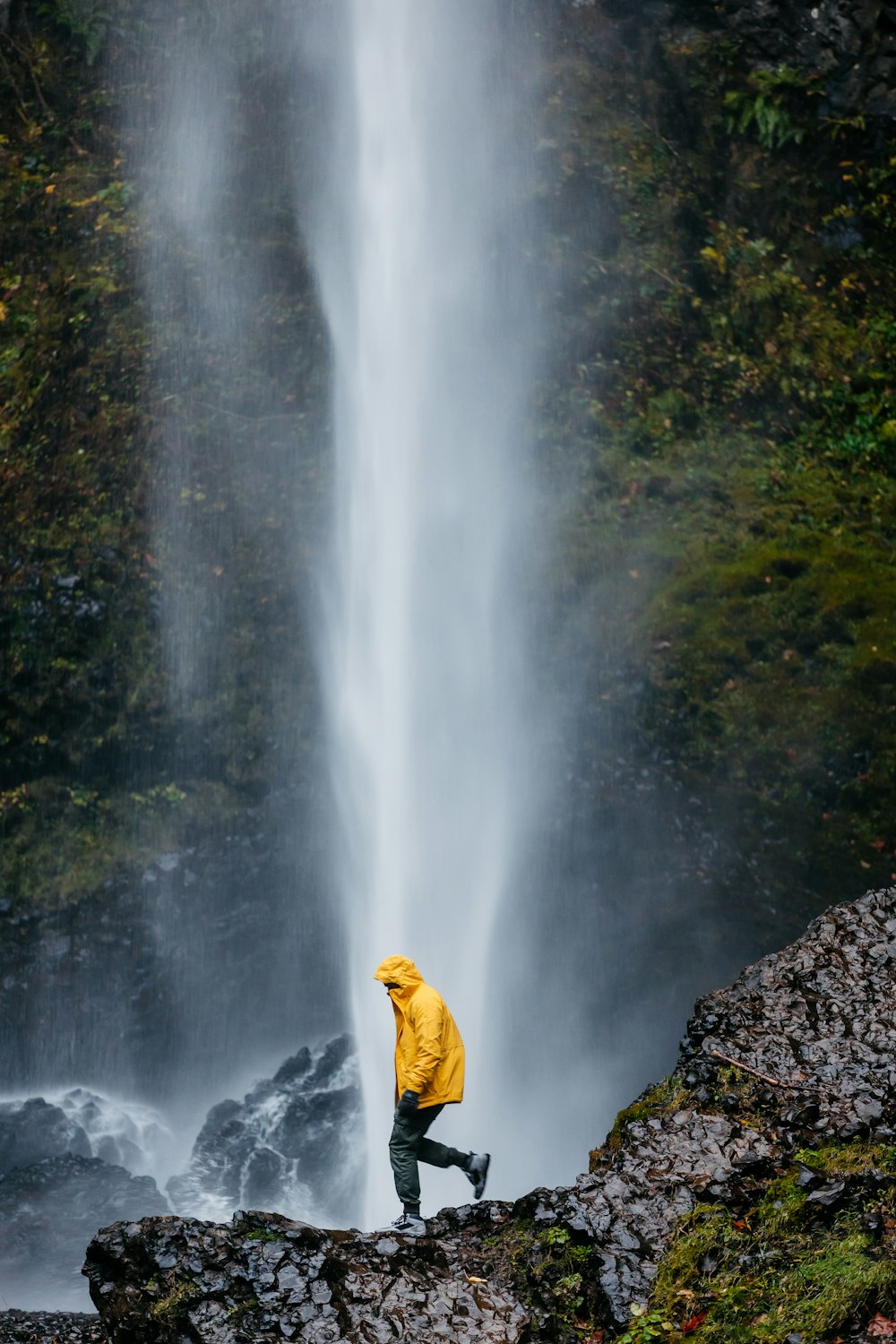 a person in a yellow jacket standing in front of a waterfall