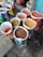 Several open bags filled with various grains and pulses are arranged on a concrete floor. The bags are colorful and patterned, indicating different brands or types of grains. The contents include lentils and other types of seeds or grains. The setting appears to be a marketplace or shop.