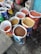 Several open bags filled with various grains and pulses are arranged on a concrete floor. The bags are colorful and patterned, indicating different brands or types of grains. The contents include lentils and other types of seeds or grains. The setting appears to be a marketplace or shop.