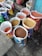 Several open bags filled with various grains and pulses are arranged on a concrete floor. The bags are colorful and patterned, indicating different brands or types of grains. The contents include lentils and other types of seeds or grains. The setting appears to be a marketplace or shop.