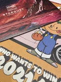 The image features a collection of promotional materials. At the top, there is a Coca-Cola Creations Stardust Limited Edition display with a red outer space theme, including celestial bodies and what appears to be a rocky planetary surface. Below it, there is a colorful cartoon character in blue overalls holding a clock, with part of a car wheel visible in the background. There is also a bold text message suggesting participation in an event or contest with large numbers '2021'.