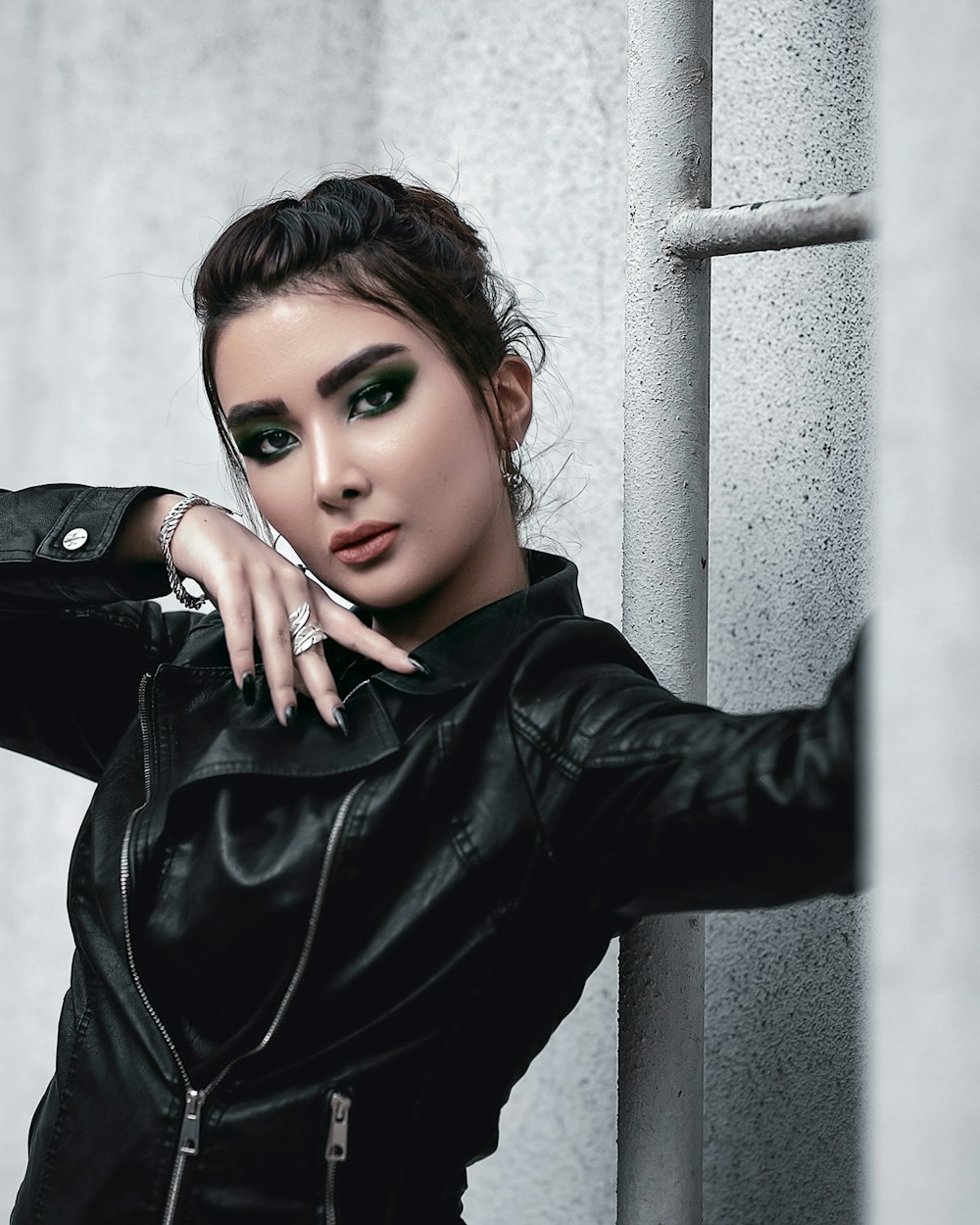 a woman in a black leather jacket leaning against a wall