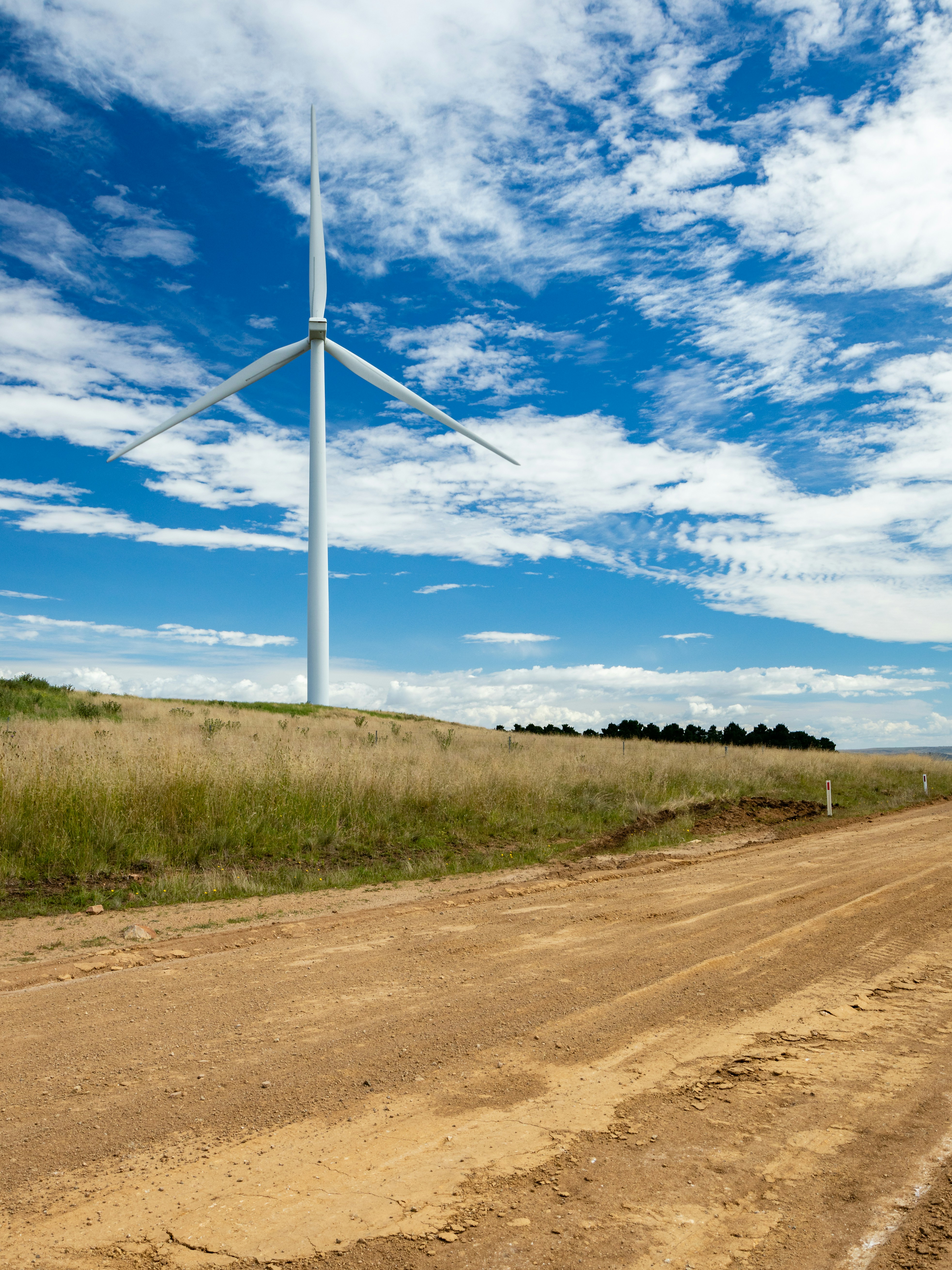 a dirt road with a wind turbine in the background