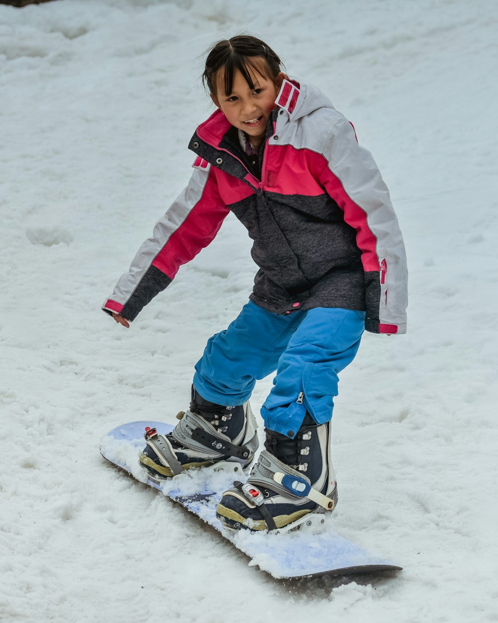 a young girl riding a snowboard down a snow covered slope