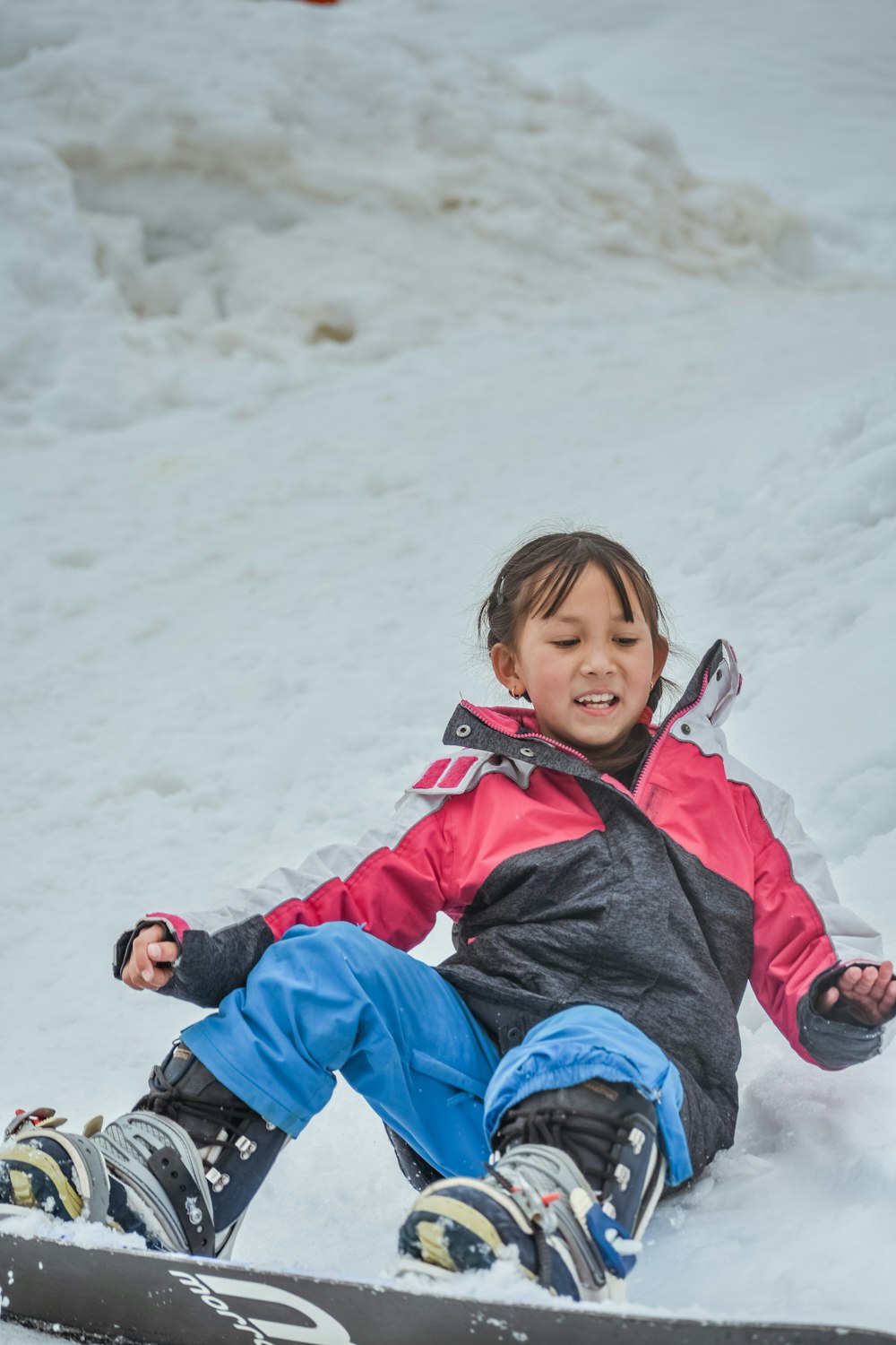 a little girl sitting in the snow on a snowboard