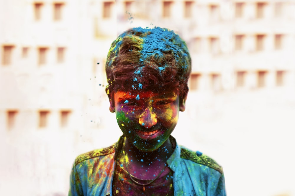 a young man covered in colored powder standing in front of a building
