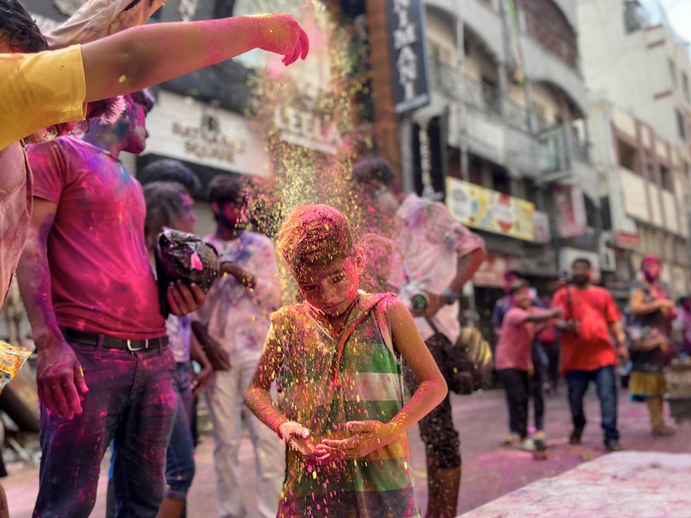 a little girl covered in colored powder standing in front of a group of people