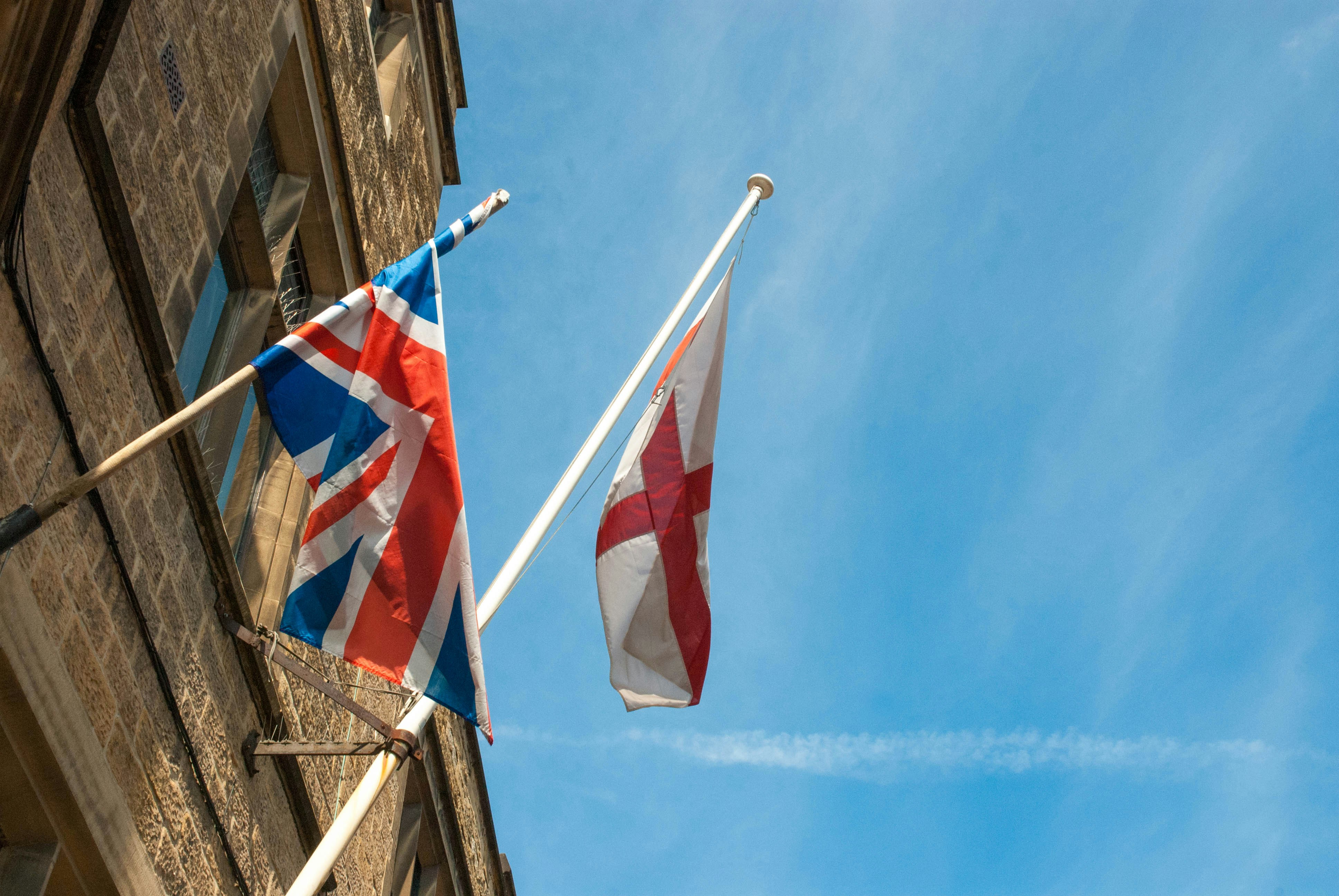 Two flags are flying in front of a building photo – Free Flag Image on ...