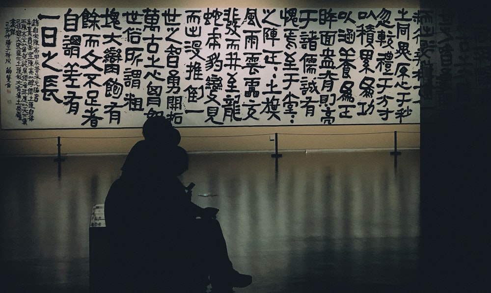 a person sitting in a chair in front of a wall with writing on it
