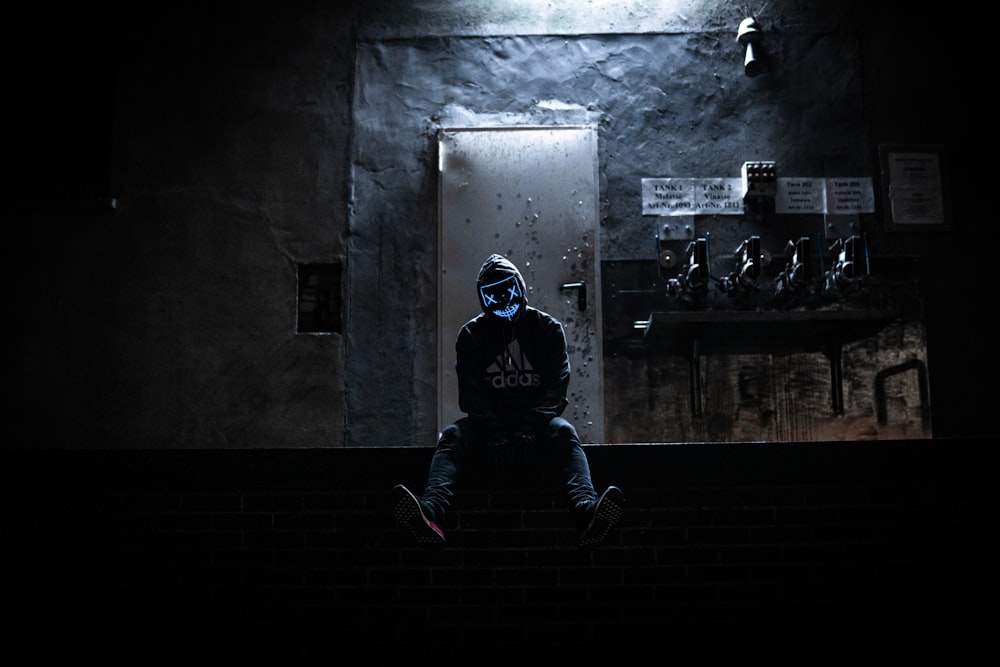 a man in a dark room sitting on a ledge