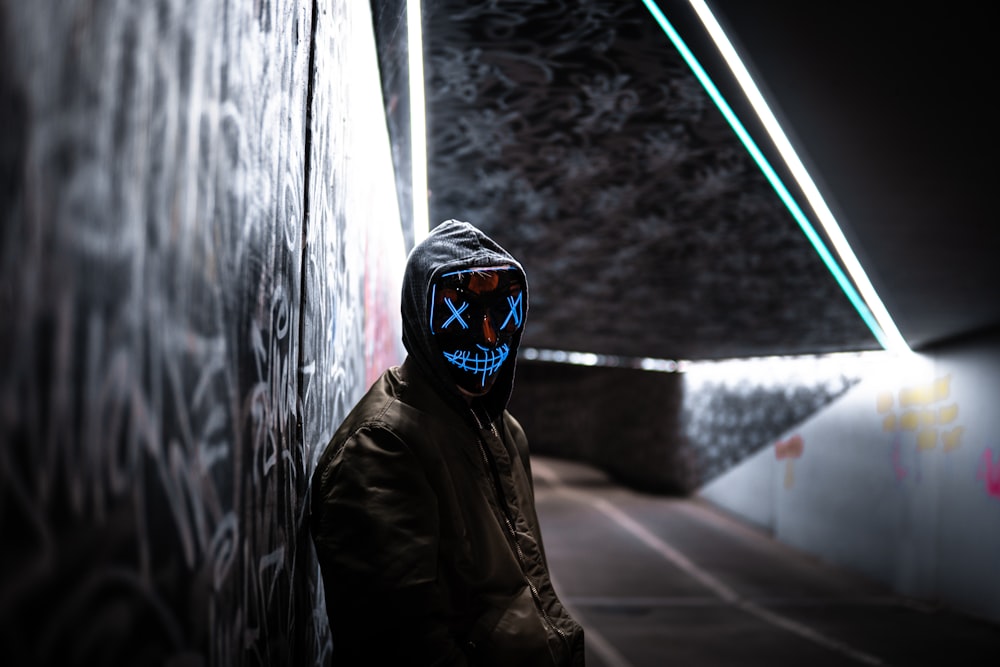 a man wearing a mask standing next to a wall