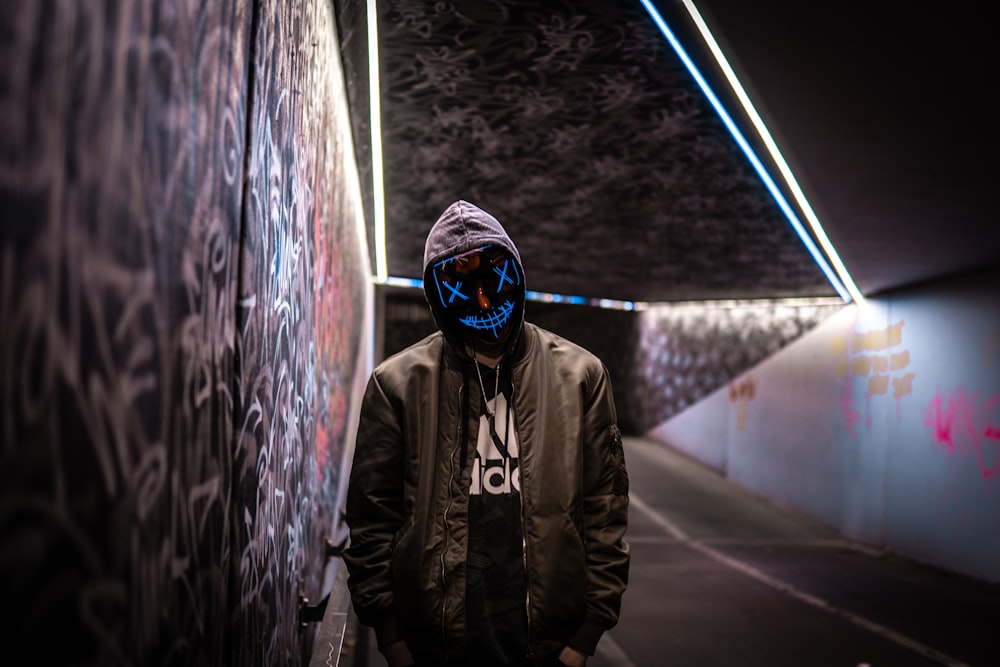 a man wearing a neon mask standing in a tunnel