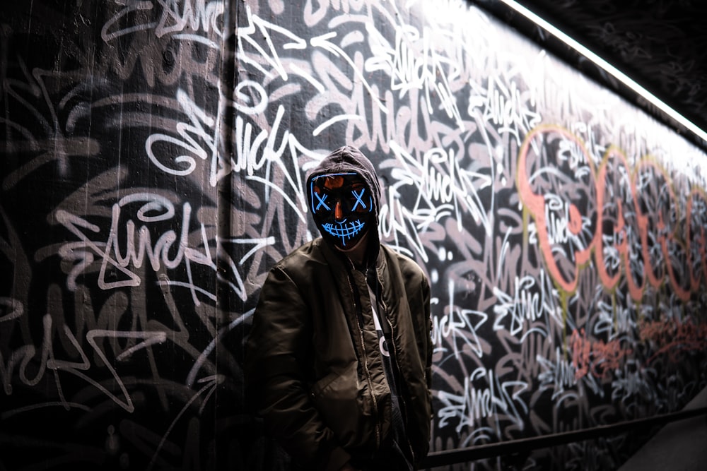 a man wearing a mask standing in front of a wall covered in graffiti