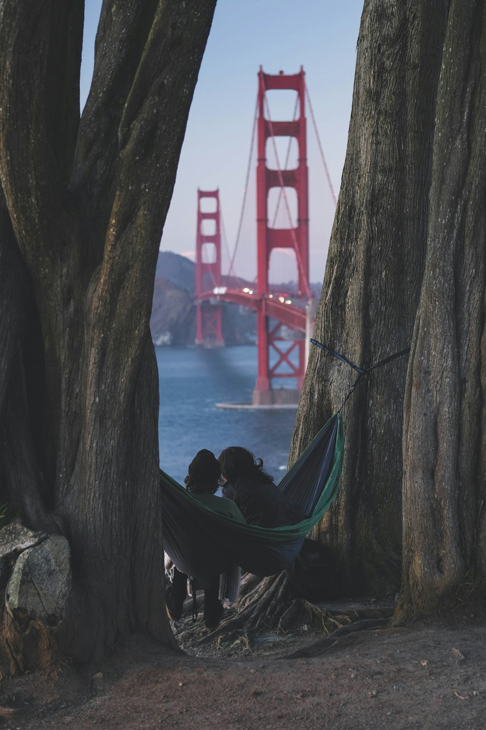 two people sitting in a hammock in front of the golden gate bridge