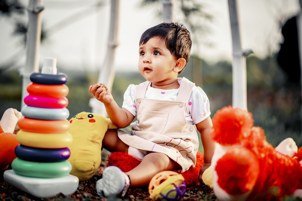 a little girl sitting on the ground next to a pile of toys