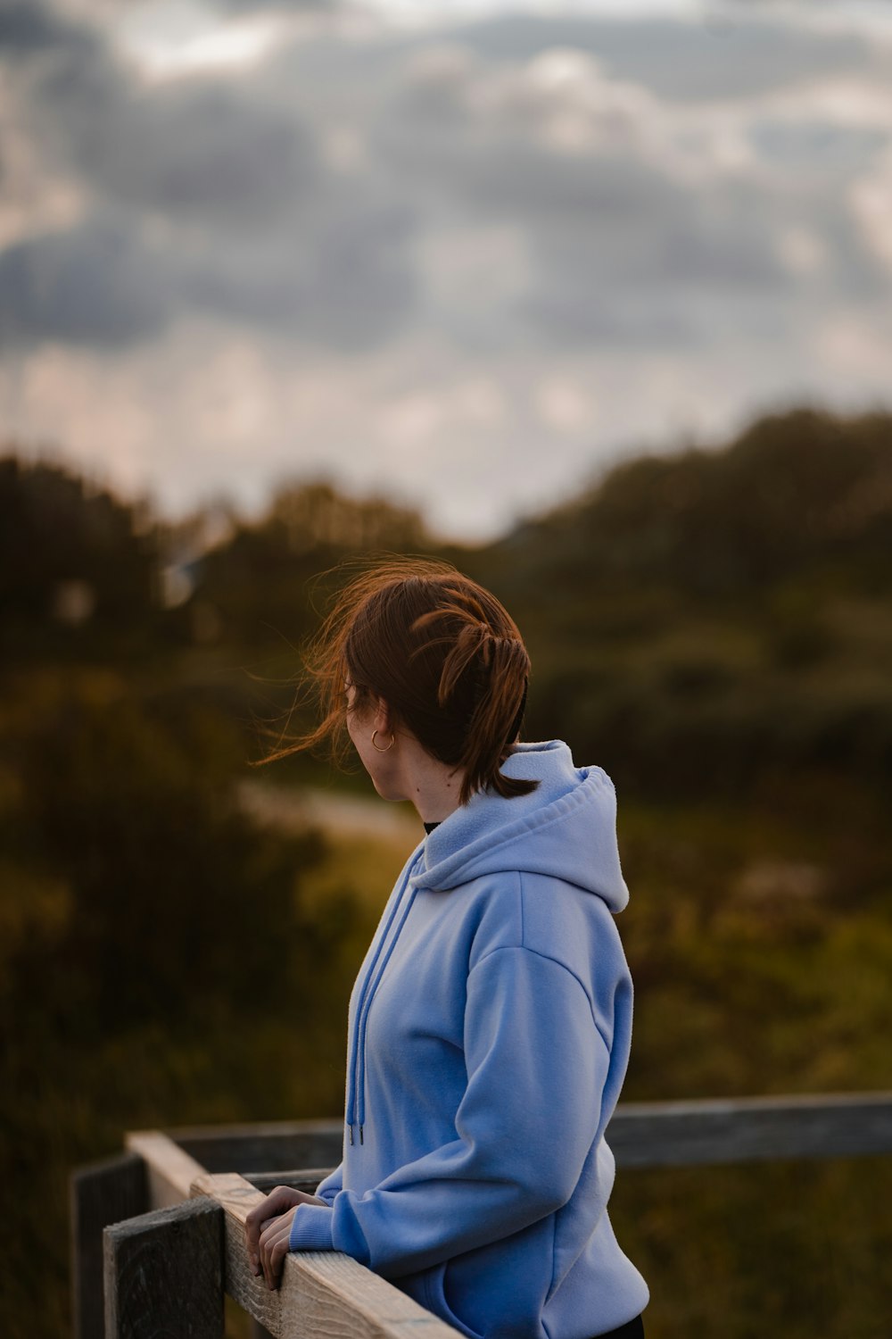 a woman in a blue hoodie looking over a fence