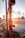A red fire hydrant with peeling paint is leaking water, creating splashes in the air against the backdrop of a sunset. The sunlight creates a warm glow and lens flare effect around the hydrant.